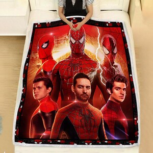 Puede incluir: Una manta roja y negra con tem&aacute;tica de Spider-Man que presenta m&uacute;ltiples im&aacute;genes de personajes de Spider-Man. La manta tiene un borde negro con detalles de rosas rojas. La manta est&aacute; sobre una cama blanca.