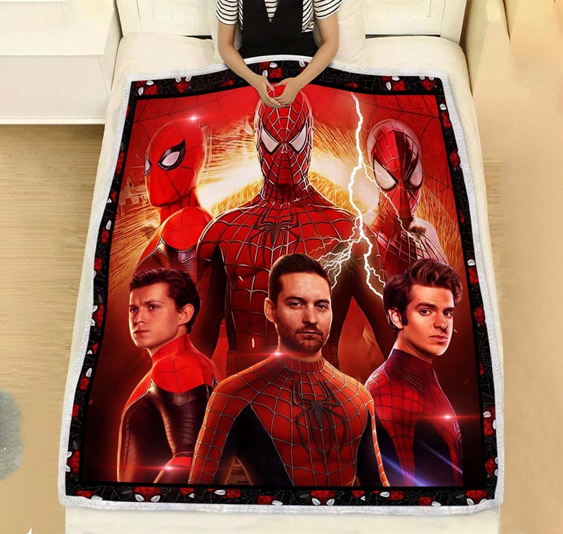 Puede incluir: Una manta roja y negra con tem&aacute;tica de Spider-Man que presenta m&uacute;ltiples im&aacute;genes de personajes de Spider-Man. La manta tiene un borde negro con detalles de rosas rojas. La manta est&aacute; sobre una cama blanca.
