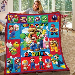 May include: A colourful Super Mario themed quilt featuring characters from the video game series. The quilt has the name "GABRIEL" and is surrounded by a red border. The quilt is made of a soft material. The quilt is a vibrant mix of red, blue, and yellow.