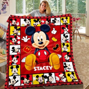 May include: A red, black, and yellow Mickey Mouse blanket. The blanket features a large image of Mickey Mouse in the centre, surrounded by smaller images of Mickey in various poses. The name "STACEY" is printed on the blanket.