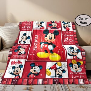 Puede incluir: Una manta roja y blanca con el tema de Mickey Mouse. La manta presenta m&uacute;ltiples im&aacute;genes de Mickey Mouse en varias poses, con la palabra "MADRE" y otro texto. La manta est&aacute; sobre un sof&aacute; beige.