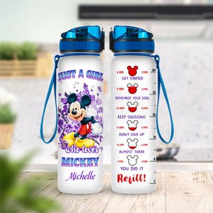 Op de afbeelding: Witte waterfles met een blauwe dop en riem, met Mickey Mouse en de tekst "Just a Girl who loves Mickey Michelle". De fles heeft een hydratatie tracker met motiverende zinnen en metingen.