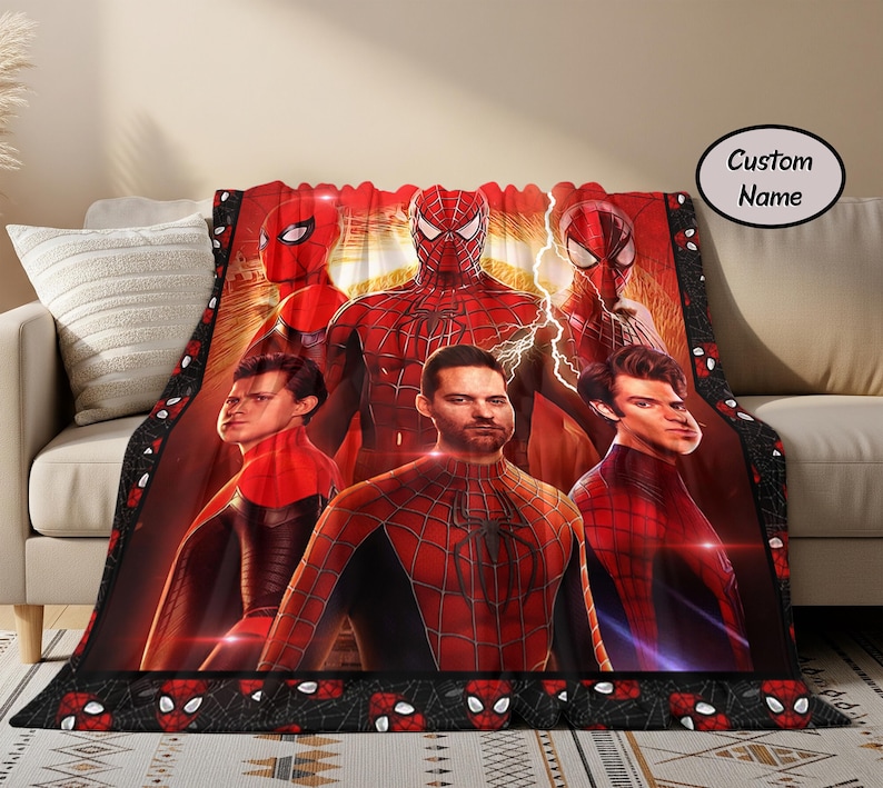 Puede incluir: Una manta roja y negra con tem&aacute;tica de Spider-Man que presenta m&uacute;ltiples personajes de Spider-Man. La manta tiene un borde negro con dise&ntilde;os de m&aacute;scaras de Spider-Man. El fondo es un degradado rojo y naranja.