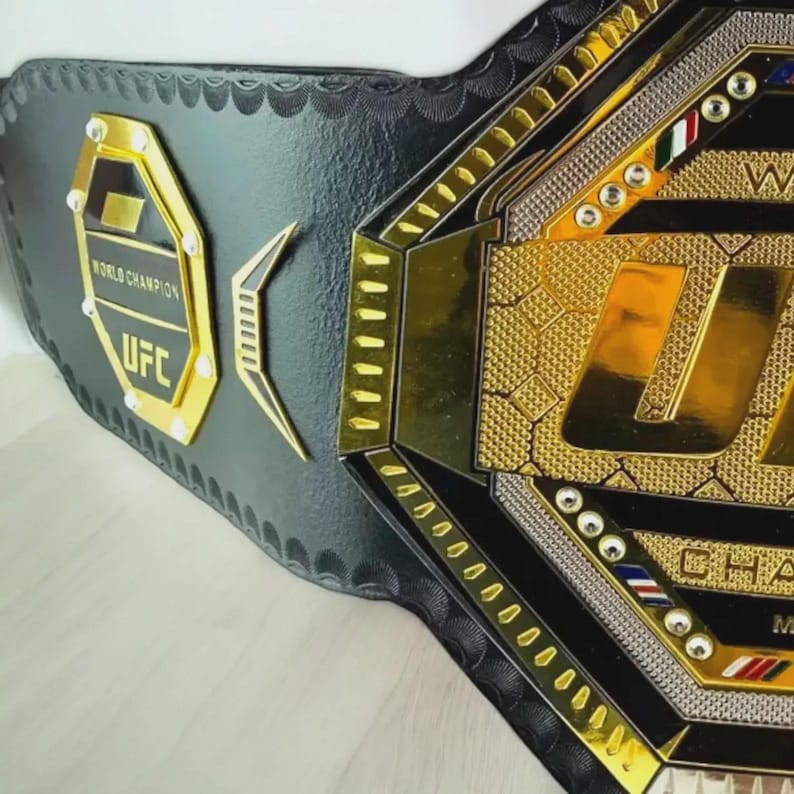 以下が含まれることがあります： 黒と金のUFCワールドチャンピオンベルト。ベルトは金のアクセント、UFCのロゴ、そして「ワールドチャンピオン」の文字が特徴です。ベルトは黒革製で、詳細なデザインが施されています。