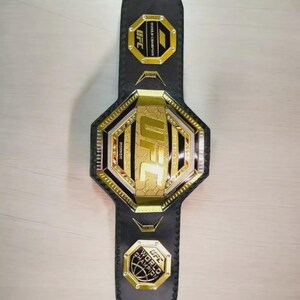 以下が含まれることがあります： 黒革のUFCワールドチャンピオンベルト。 金と銀のアクセントが施されています。 ベルトにはUFCのロゴと「WORLD CHAMPION」の文字が前面と端にあります。 中央のプレートは八角形です。