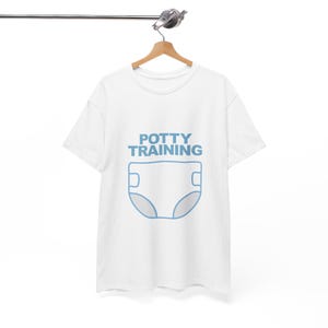 May include: White t-shirt with the words "POTTY TRAINING" in light blue above a light blue diaper graphic. The shirt is hanging on a wooden hanger.