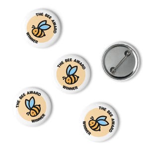 May include: A collection of white pinback buttons with a cartoon bee design. Each button features a yellow circle with a black and yellow bee, blue wings, and the text "THE BEE AWARD WINNER". One button shows the back with a pin.
