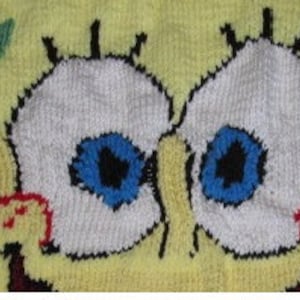 May include: Close-up of a yellow knitted fabric with a cartoon character's eyes. The eyes are white with blue pupils and black eyelashes. The fabric is textured and has a slightly bumpy surface.