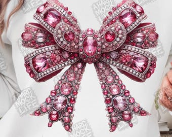 May include: A pink jeweled bow design on a white sweatshirt. The bow features various sizes of pink gems and rhinestones. The text "A HARD MOCK LIFE" is printed around the bow.
