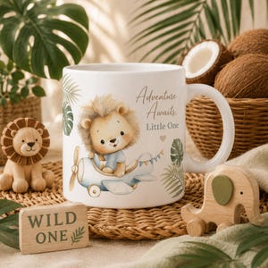 Puede incluir: Una taza de cer&aacute;mica blanca con un le&oacute;n de dibujos animados en un avi&oacute;n azul claro con el texto Adventure Awaits, Little One. La taza est&aacute; rodeada por una figura de le&oacute;n de madera, un juguete de elefante de madera y un bloque con el texto WILD ONE.