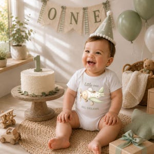 Baby first birthday mockup featuring Green Teddy Bear Clipart airplane illustration on a white bodysuit with sage green party decorations, nursery styling and baby boy birthday inspiration.