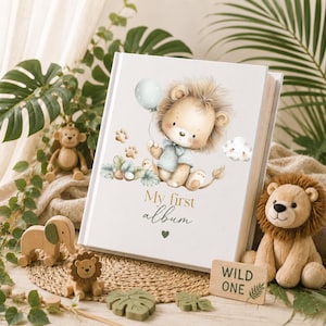 Puede incluir: Un &aacute;lbum de fotos blanco con una ilustraci&oacute;n en acuarela de un cachorro de le&oacute;n sosteniendo un globo azul claro, rodeado de huellas y hojas. El texto My first album aparece en letras doradas y negras con un peque&ntilde;o coraz&oacute;n verde debajo.