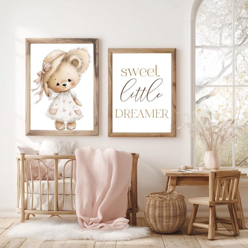 Peut inclure: Deux impressions encadr&eacute;es sur le th&egrave;me de la chambre d'enfant. L'une pr&eacute;sente une illustration &agrave; l'aquarelle d'un ours en peluche portant un chapeau et une robe. L'autre impression dit "sweet little dreamer" en lettres dor&eacute;es. Un berceau en bois, une couverture et un tapis sont au premier plan.