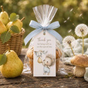 May include: A clear plastic treat bag containing a muffin, tied with a light blue ribbon and a rectangular tag. The tag features the text Thank you for being with us on this special day and an illustration of a hedgehog holding a yellow pear.