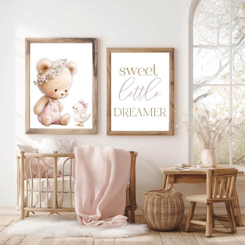 May include: Two framed prints with a nursery theme. One print features a watercolor illustration of a teddy bear and a chick. The other print says "sweet little dreamer". A crib, blanket, and small table are also in the image.