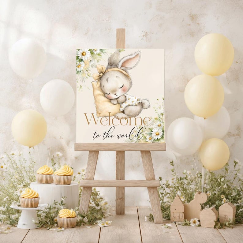 May include: A baby shower sign on a wooden easel features a sleeping bunny illustration with the text "Welcome to the world." The sign is surrounded by balloons, cupcakes, and floral arrangements in soft pastel colors, creating a gentle and welcoming atmosphere.