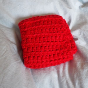 May include: A red crocheted square pillow or cushion. The pillow is made with a simple stitch and has a soft, textured surface.