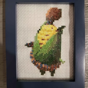 May include: A framed cross-stitch of a green and yellow creature with brown accents. The creature is standing on its hind legs and has a yellow and green patterned body.