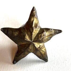 May include: A bronze-coloured, five-pointed star. The star has a textured surface and a slightly tarnished appearance. The star is likely a decorative object or part of a larger design.