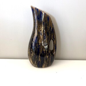 May include: A small, blue and brown ceramic vase with a unique, speckled glaze. The vase has a rounded, teardrop shape with a narrow neck and a handle.