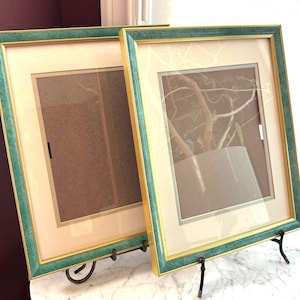 May include: Two rectangular picture frames featuring a textured teal green finish with thin gold inner and outer edges. Each frame includes a cream-coloured mat board surrounding a brown backing board, protected by a clear glass front panel.