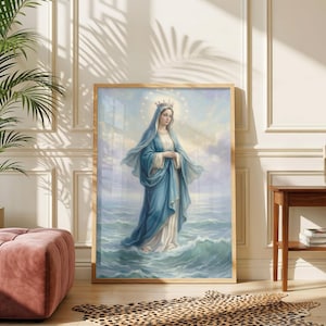 Op de afbeelding: Een ingelijste prent van een religieuze figuur in een blauwe jurk en kroon, staand in het water. Het kunstwerk is geplaatst in een lichtgevende scène, omlijst door licht hout. De prent wordt getoond in een kamer met een roze poef en een luipaardprint tapijt.