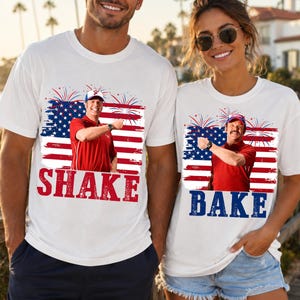 Pode incluir: Duas t-shirts brancas com um gráfico de um homem de camisa vermelha e boné azul sobre um fundo de bandeira americana com fogo de artifício. A t-shirt da esquerda tem o texto vermelho SHAKE e a da direita o texto azul BAKE sob o gráfico.