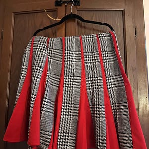 May include: A black and white houndstooth skirt with red panels. The skirt is pleated and has a flared silhouette.
