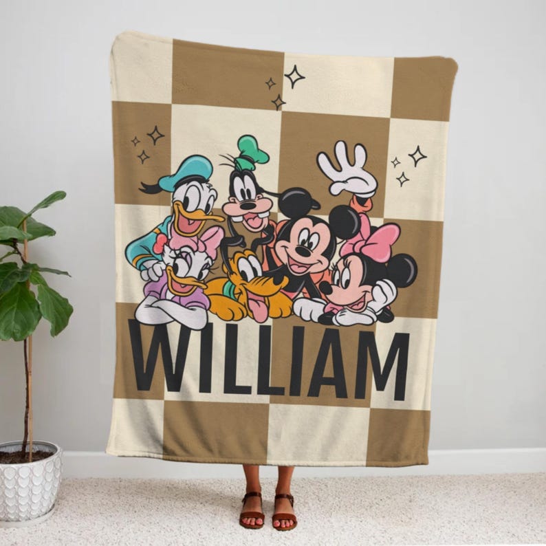 Puede incluir: Una manta a cuadros marr&oacute;n y beige con personajes de dibujos animados de Disney, como Mickey y Minnie Mouse, Donald y Daisy Duck, Goofy y Pluto. El nombre "WILLIAM" est&aacute; impreso en letras negras grandes.