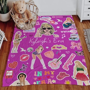 May include: A vibrant purple blanket featuring various illustrations and text, including a woman wearing sunglasses, guitars, hearts, and the words "Kyleigh's Era" and "In My Era".