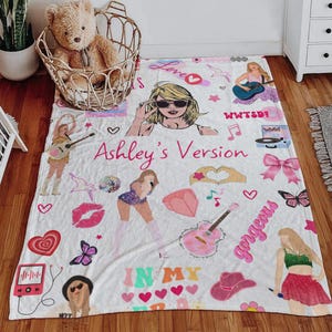 May include: White blanket with illustrations of a pop star, musical notes, hearts, and the text "Ashley's Version" in pink. The blanket features a cartoon image of a woman wearing sunglasses and holding a guitar.