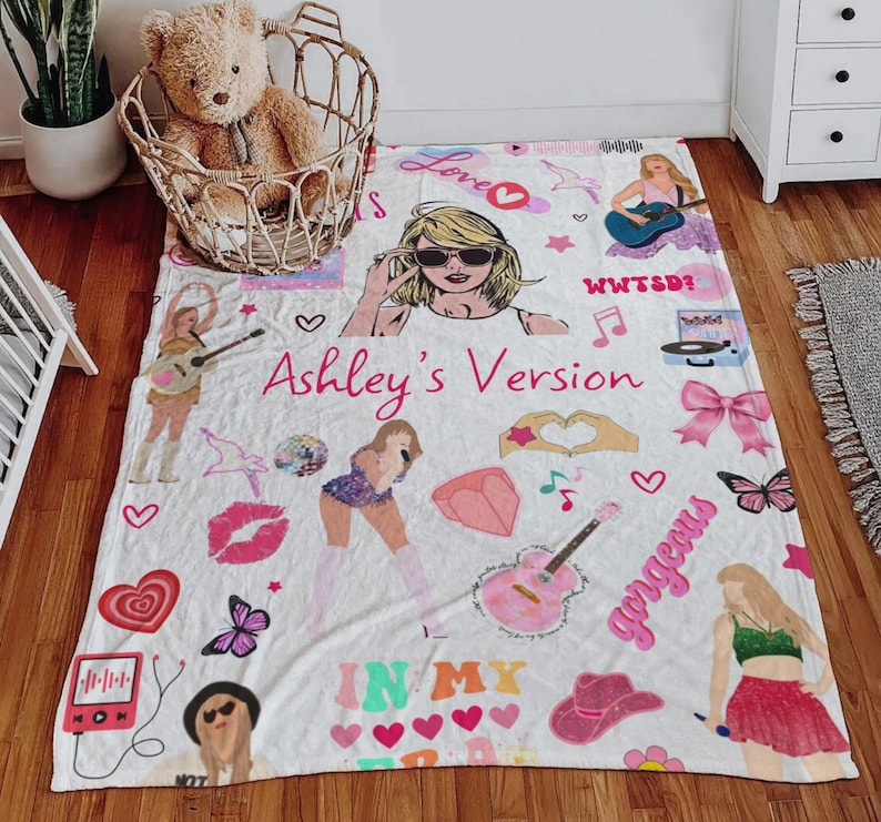 May include: White blanket with illustrations of a pop star, musical notes, hearts, and the text "Ashley's Version" in pink. The blanket features a cartoon image of a woman wearing sunglasses and holding a guitar.