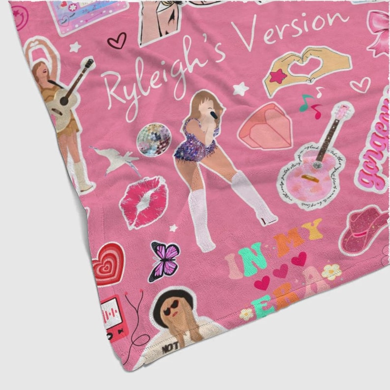 May include: Pink blanket with a repeating pattern of illustrations and text. The design includes images of a woman singing, guitars, hearts, butterflies, and the words "Ryleigh's Version" and "In My Era."