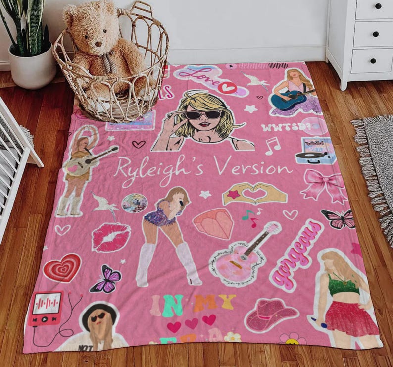 May include: Pink blanket with illustrations of a woman, musical instruments, hearts, and the text "Ryleigh's Version". The blanket has a variety of graphics and the word "gorgeous".
