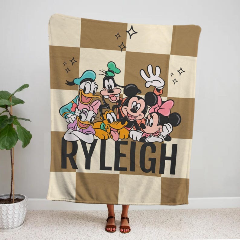 Puede incluir: Una manta a cuadros beige y crema con los personajes de Disney Mickey Mouse, Minnie Mouse, Donald Duck, Daisy Duck, Goofy y Pluto. El nombre "RYLEIGH" est&aacute; impreso en letras negras grandes.