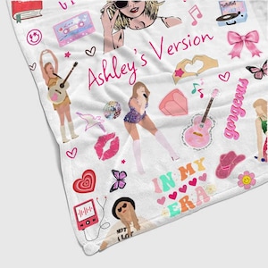 May include: White blanket with colorful illustrations and the text "Ashley's Version" in pink. The blanket features drawings of a singer, musical notes, hearts, a guitar, and the words "In My Era".