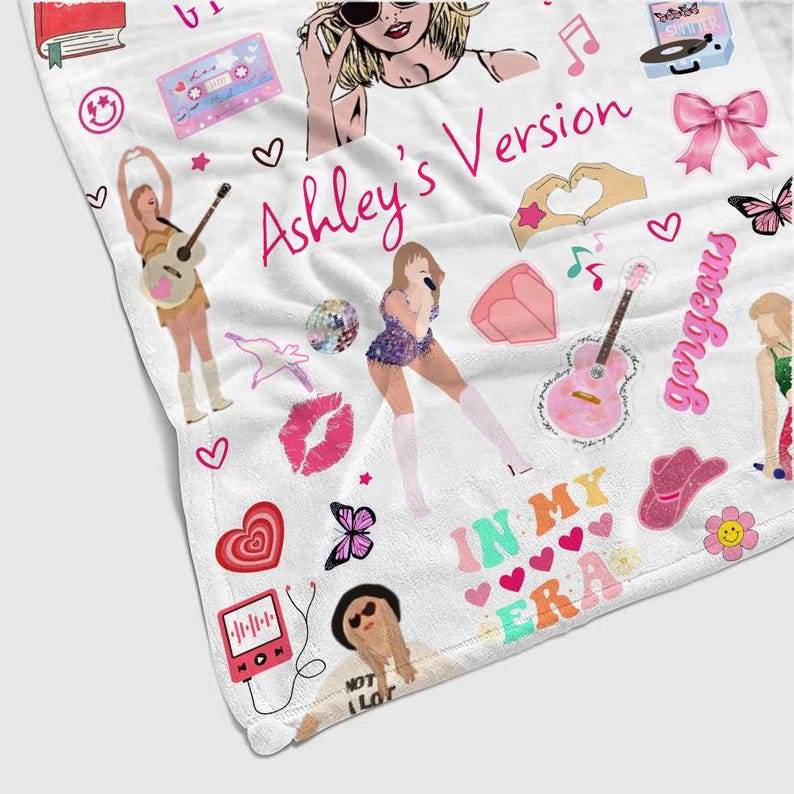 May include: White blanket with colorful illustrations and the text "Ashley's Version" in pink. The blanket features drawings of a singer, musical notes, hearts, a guitar, and the words "In My Era".
