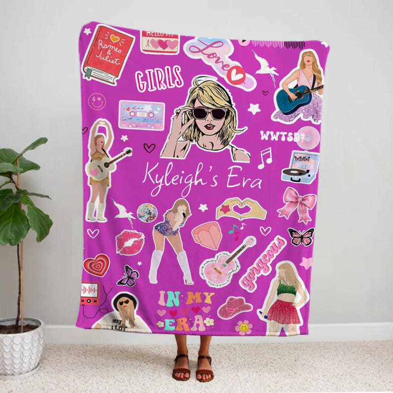 May include: A magenta blanket featuring various illustrations and text, including a woman with sunglasses, guitars, hearts, and the words "Kyleigh's Era," "Girls," and "In My Era." The blanket is a vibrant and colorful accessory.