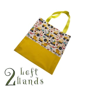 May include: A yellow tote bag with a white fabric lining. The lining features a pattern of yellow construction vehicles on a white background. The bag has a yellow fabric handle.
