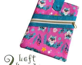 May include: A pink fabric crossbody bag with a repeating pattern of teal foxes, flowers, and foliage. The bag has a teal strap, a gold zipper, and a teal button closure. The text "2 Left Hands" is written in green script.