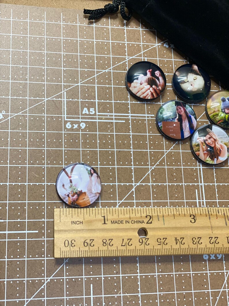 Peut inclure: Un ensemble de six ornements photo ronds en verre avec diff&eacute;rentes images. Les ornements mesurent environ 2,5 cm de diam&egrave;tre et sont pr&eacute;sent&eacute;s sur un tapis de coupe brun avec une r&egrave;gle.