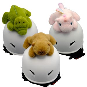 May include: Three white helmets with different plush animal toppers. The first helmet has a green alligator topper, the second has a brown bear topper, and the third has a pink unicorn topper.