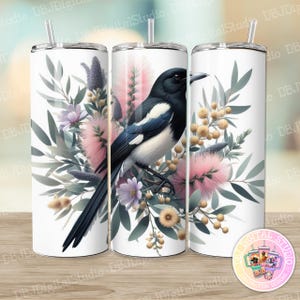 Può includere: Un bicchiere bianco con un uccello gazza bianco e nero circondato da fiori rosa e verdi. Il bicchiere ha una cannuccia e un coperchio.