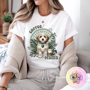 Puede incluir: Camiseta blanca con un gráfico de un cachorro Cavapoo con un collar verde en forma de corazón, rodeado de hojas verdes y las palabras "Coffee Lover Cavapoo Mama". Una taza de café está al lado del cachorro.