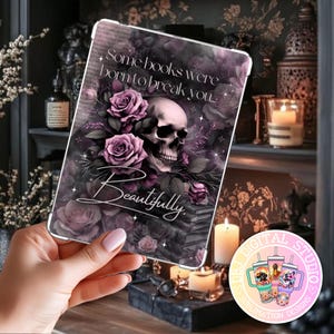 May include: A tablet case featuring a skull, roses, and the text "Some books were born to break you... Beautifully." The design incorporates shades of purple, black, and white, creating a gothic aesthetic. The case is held in a person's hand.