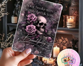 Puede incluir: Una funda para tableta con un diseño gótico, que presenta una calavera, rosas y el texto "Some books were born to break you... Beautifully." El diseño utiliza tonos de morado, negro y blanco. La funda se sostiene en una mano.