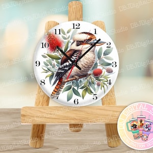 May include: A white clock face with black Roman numerals and a kookaburra bird illustration. The clock is on a wooden easel.
