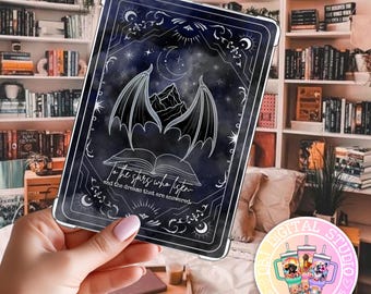 May include: A dark blue phone case featuring a celestial design with a mountain, bat wings, and moon. The case has the text "To the stars who listen and the dreams that are answered." The case is held in front of a bookshelf.