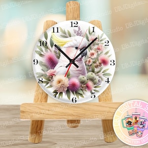 May include: A white cockatoo with pink accents sits on a branch with pink and green flowers. The cockatoo is on a white clock face with black Roman numerals and black hands. The clock is on a wooden easel.