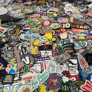 Peut inclure: Une grande collection d'écussons en tissu brodé assortis de formes, tailles et couleurs variées. Les écussons présentent divers motifs, notamment des drapeaux américains, du texte, des animaux, des logos et des illustrations.